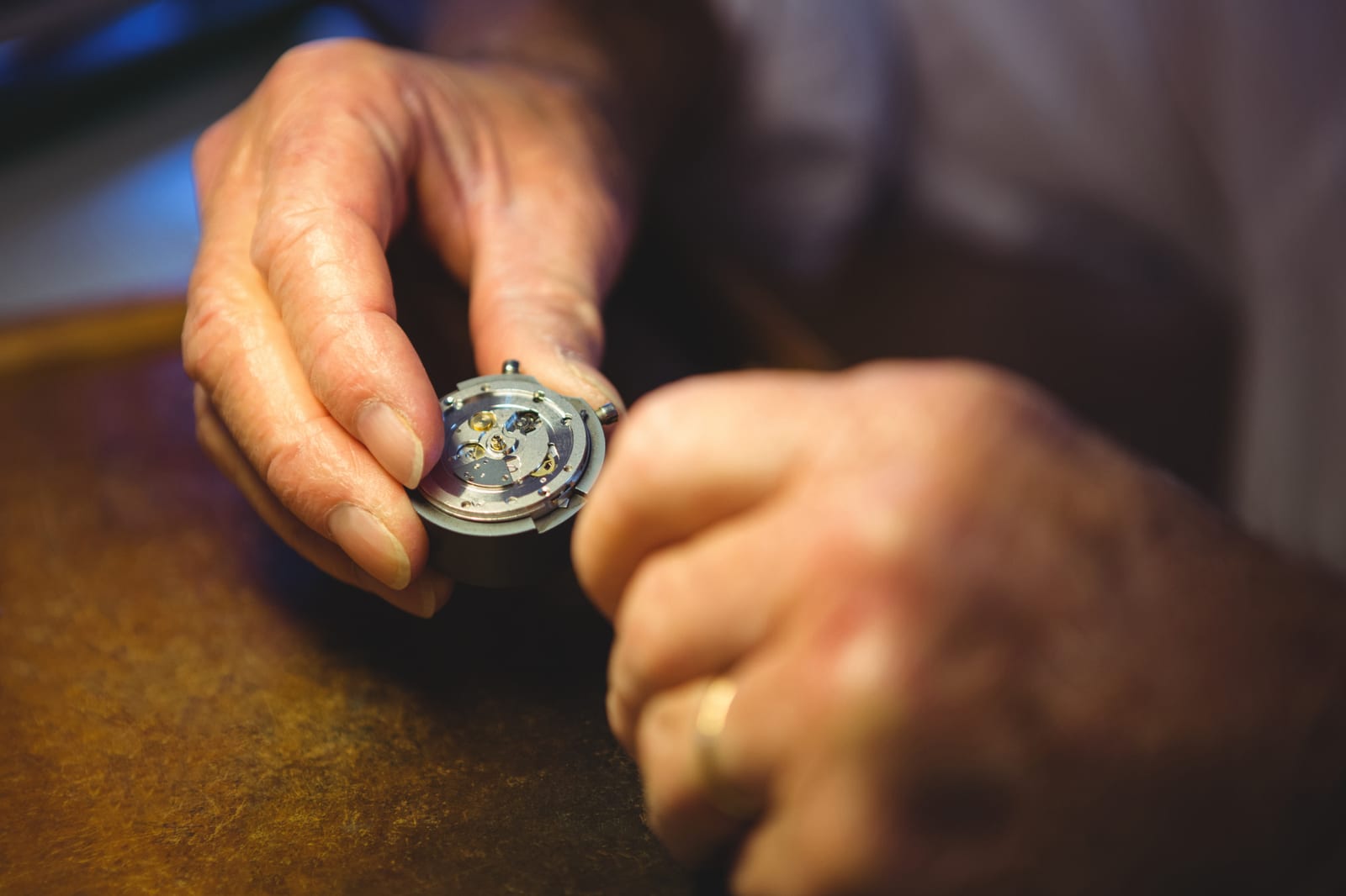 Mani al lavoro con pinzette su un movimento di orologio aperto