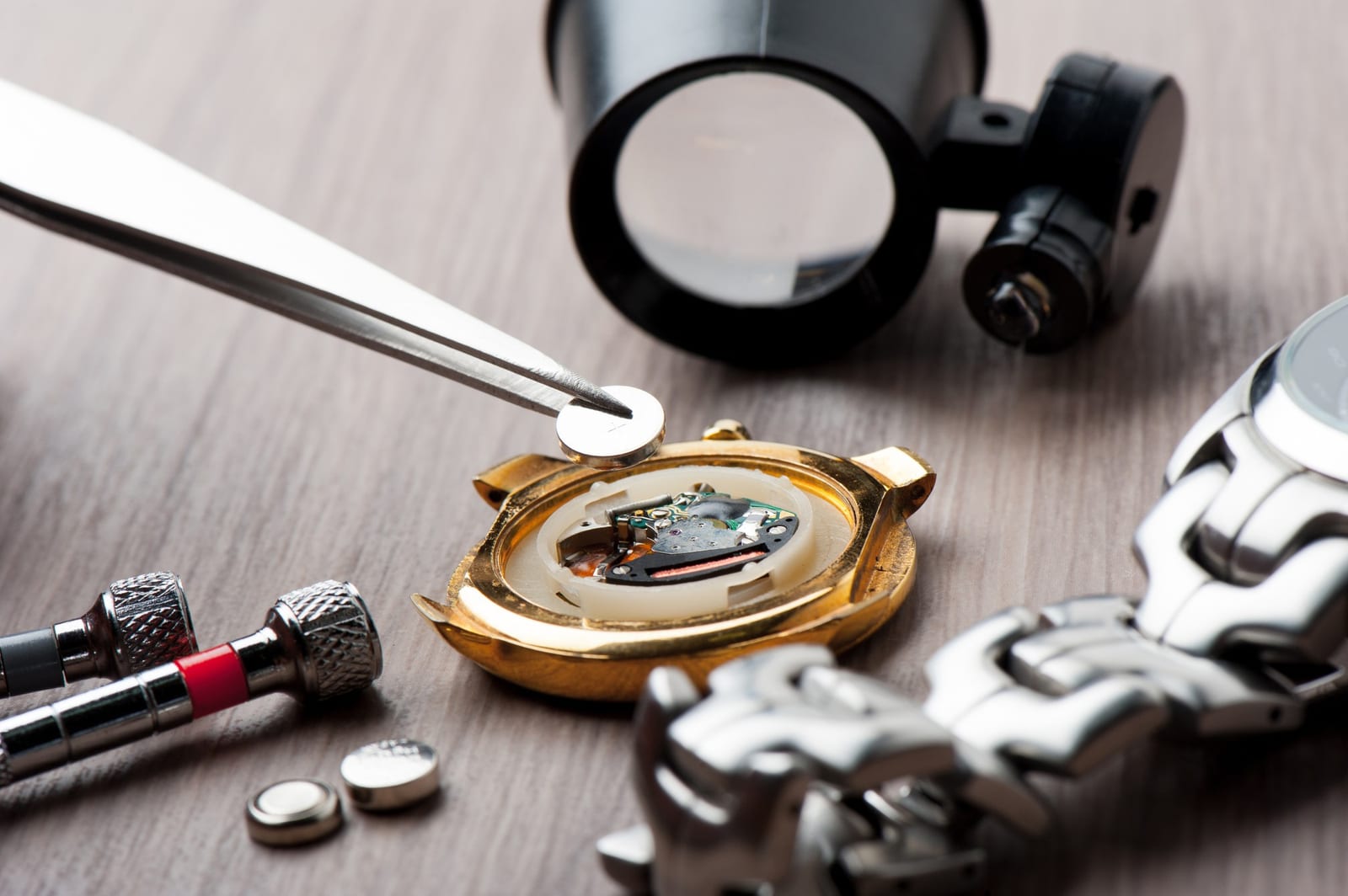 Lente, cacciavite e cassa di orologio aperta con bracciale, pronti per la lavorazione